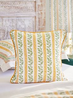 a white bed topped with pillows next to a wooden headboard covered in green and yellow striped sheets