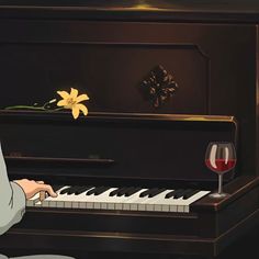 a person sitting at a piano with a glass of wine in front of it and a flower on top of the piano