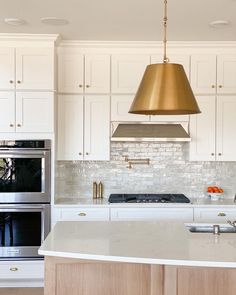 a kitchen with white cabinets and an island in front of a stove top oven under a gold pendant light