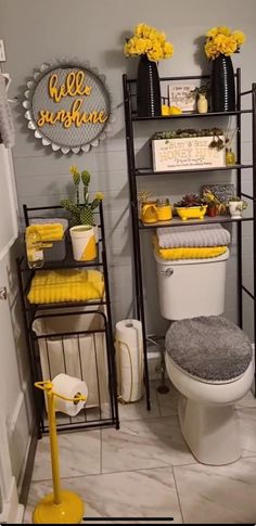 a bathroom decorated in yellow and gray with flowers on the shelves above the toilet, along with other decorations