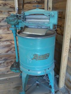 an old blue machine sitting inside of a wooden building next to a wall with wood planks on it