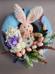 a knitted bunny sitting on top of a wreath with flowers and eggs in it