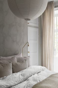 a white bed sitting under a window next to a lamp in a room with curtains