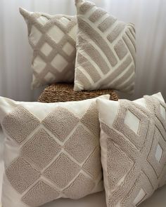 three pillows sitting on top of a bed next to a wicker basket and window