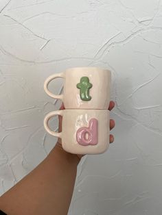 two coffee mugs with the letters b and c painted on them are held up against a white wall