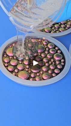 a person pouring water into a bowl filled with small round objects on top of a blue surface