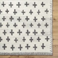 a white rug with black crosses on the bottom and grey dots in the middle, sitting on a wooden floor