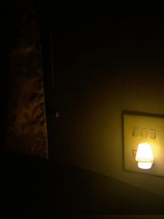 a light that is on in the dark next to a wall mounted switch box with two lights