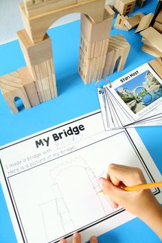 a child is making a bridge with wooden blocks and construction paper on the table next to it