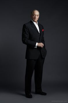 an older man in a tuxedo poses for a studio portrait with his hands on his hips