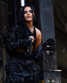 a woman with black hair and piercings on her chest, holding an umbrella while standing in front of a stage