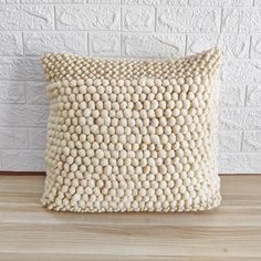 a white pillow sitting on top of a wooden floor next to a brick wall and wood floor