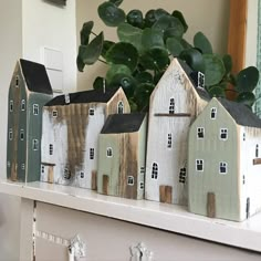 three small wooden houses sitting on top of a white shelf next to a potted plant