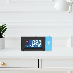 an alarm clock sitting on top of a white dresser next to a potted plant