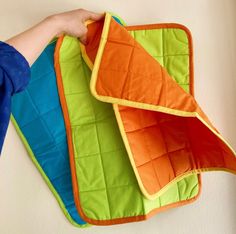 a person holding an oven mitt on top of a kitchen towel rack with three different colors