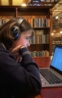 a person wearing headphones sitting in front of a laptop on a table with books