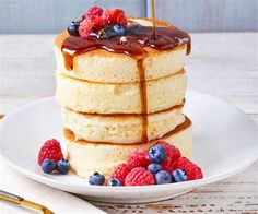 a stack of pancakes on a plate with berries and syrup being drizzled over them