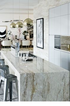 a modern kitchen with marble counter tops and white cabinets, along with bar stools