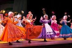 the children are dressed in colorful dresses and dancing together on stage with their hands up