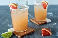 two cocktails with grapefruit, orange and lime on a wooden cutting board