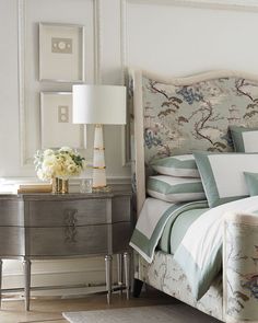 a bed with blue and white pillows in a bedroom next to a dresser, lamp and pictures on the wall