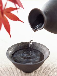 a person pouring water into a bowl with a red flower in the backgroud