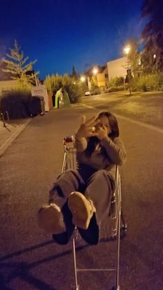 a person sitting in a shopping cart on the street at night with their hand up to their face