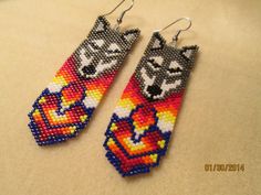 two pairs of beaded earrings with wolf and heart designs on them sitting on a table