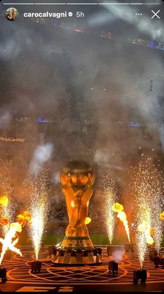 fireworks light up the night sky above a large statue in front of a stadium filled with spectators