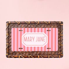 a pink and white striped name tag hanging from a bamboo frame on a pink wall