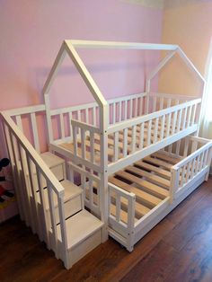 a white bunk bed with stairs and storage underneath it in a pink walled wall room