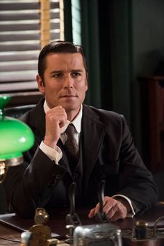 a man in a suit sitting at a desk with a green lamp on it's side