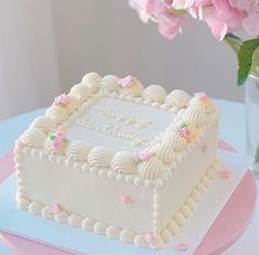 a white cake sitting on top of a table next to a vase filled with pink flowers