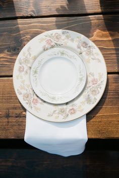 two white plates on top of each other with napkins next to them, sitting on a wooden table