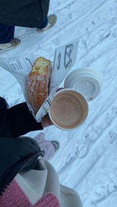 a person holding a doughnut and coffee in their hand on top of snow covered ground