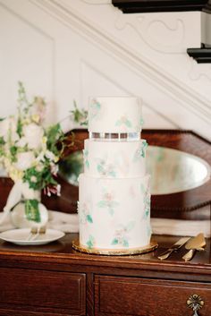 a white wedding cake sitting on top of a wooden table next to a vase with flowers