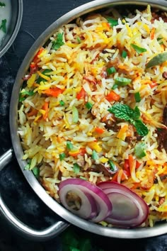 a pan filled with rice and vegetables on top of a black table next to silver spoons