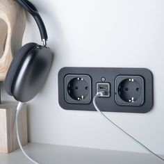 an electrical outlet with two plugs and headphones attached to the wall next to a cutting board