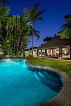 an outdoor swimming pool surrounded by palm trees and lawn furniture at night with lights on