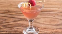 a cocktail with raspberry garnish in a glass on a wooden table