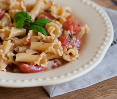 a white plate topped with pasta covered in sauce and vegetables on top of a wooden table