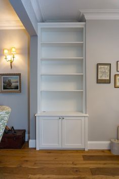 a white bookcase in the corner of a room with wood floors and pictures on the wall