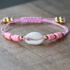 a pink and gold bracelet with a shell on the end is sitting on a wooden table