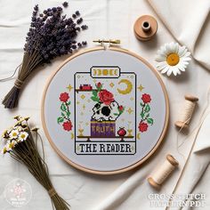 a cross stitch pattern with flowers on it and some thread spools next to it