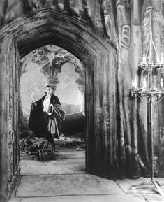 an old black and white photo of a man standing in front of a castle entrance