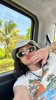 a woman sticking her tongue out in the back of a car while wearing sunglasses and a hat