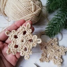 crocheted snowflakes are being held by someone's hand next to yarn and needles