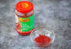 an open jar of chili paste next to a small glass bowl filled with red peppers