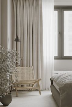 a bed sitting next to a window covered in white curtains and a plant on top of a wooden chair