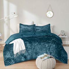 a bed with teal colored comforters and pillows in a white room next to a round mirror